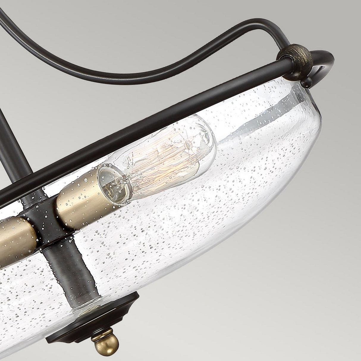 Close-up of the Griffin 3 Light Large Semi-Flush, featuring a stylish ceiling light fixture with a clear glass bowl-shaped shade and an Edison-style exposed bulb. The Palladian Bronze frame with weathered brass accents adds a modern touch against a light grey background.