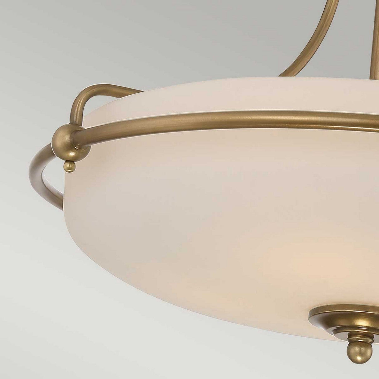The Griffin 4 Light Semi-Flush in Weathered Brass showcases a sophisticated ceiling light with a frosted glass bowl encircled by an elegantly curved weathered brass frame. Its ambient lighting offers a blend of modern elegance and vintage charm.