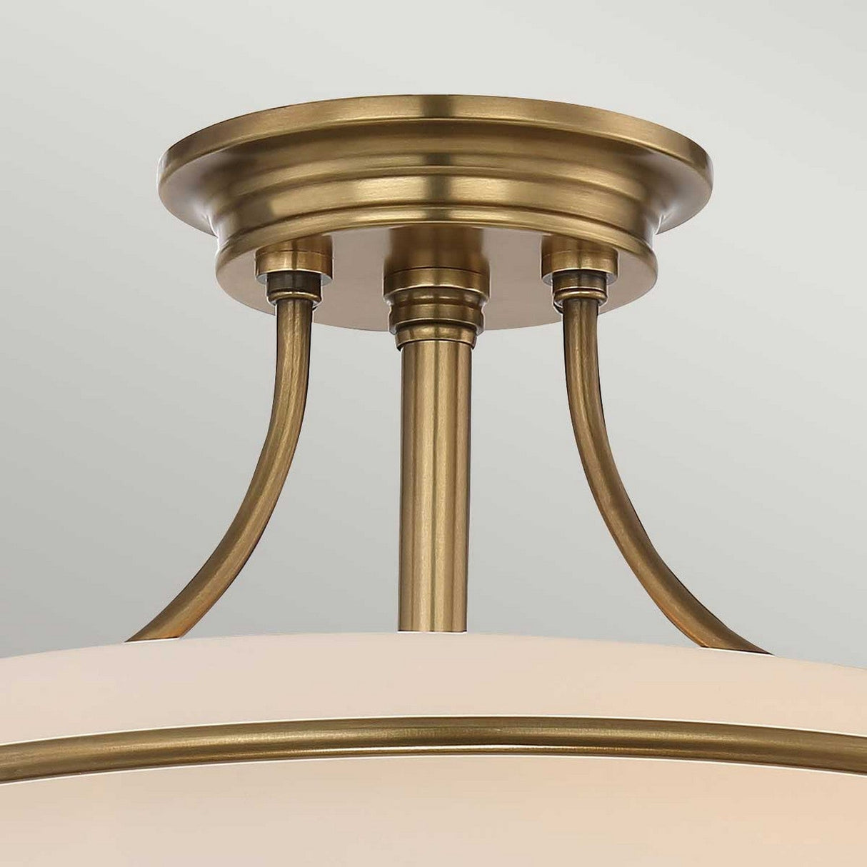 A close-up view of the Griffin 3 Light Semi-Flush with its elegantly curved metal supports and etched white shade. The fixture showcases a sleek, weathered brass finish that provides a modern yet timeless appearance.
