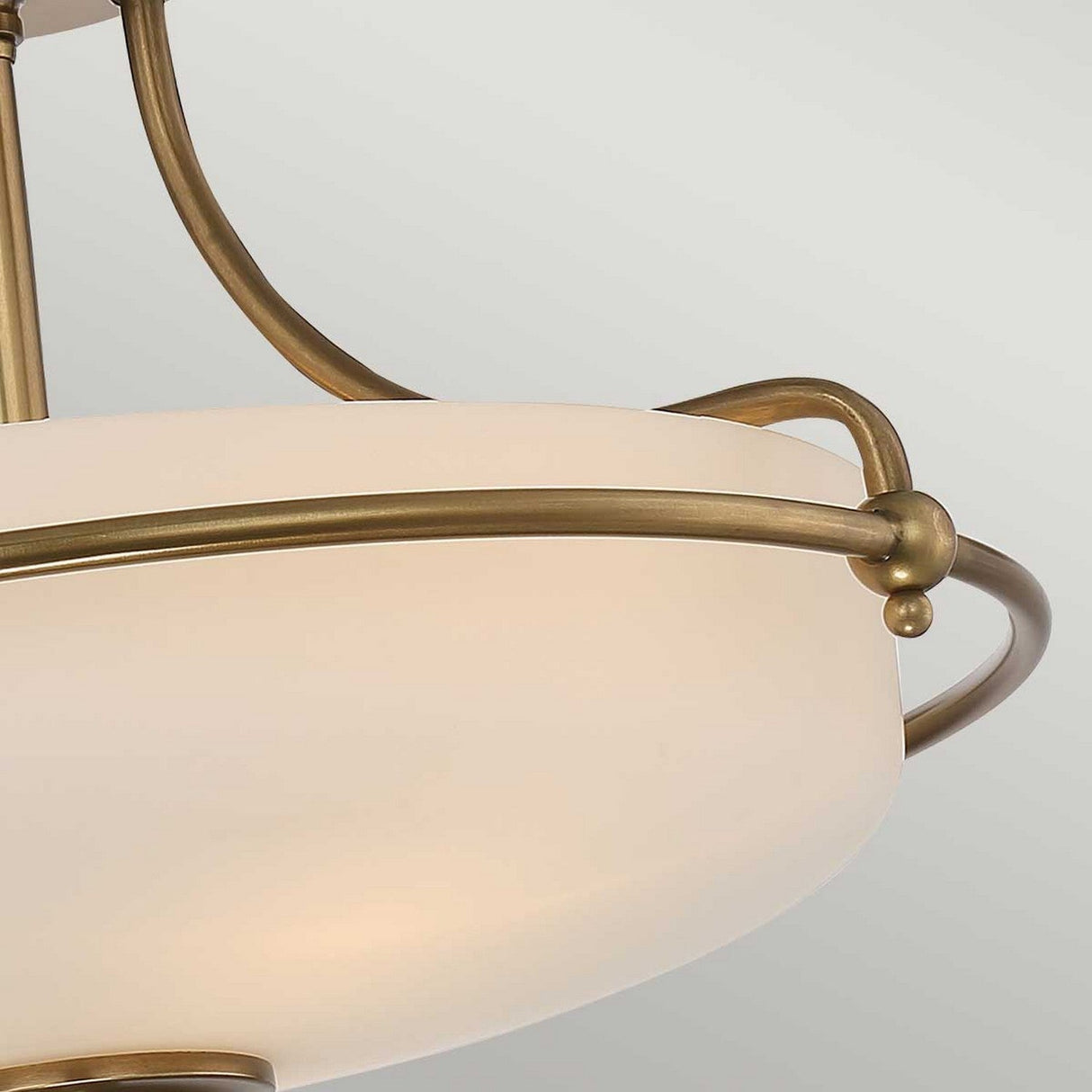 Close-up of the Griffin 3 Light Semi-Flush - Weathered Brass, showcasing its etched white shade and decorative weathered brass accents that form elegant curves. The classic and sophisticated design provides a warm glow against a neutral background.