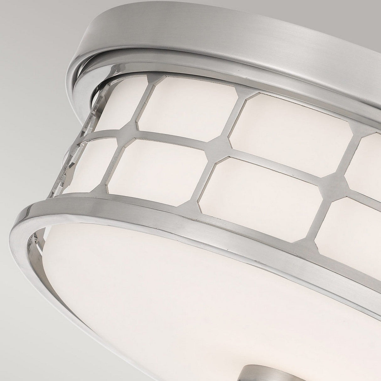 Close-up of the Guardian 2 Light Flush ceiling light fixture featuring a brushed nickel frame with a hexagonal pattern. The opal glass shade emits a soft glow, enhancing its sleek and contemporary design against a plain gray background.