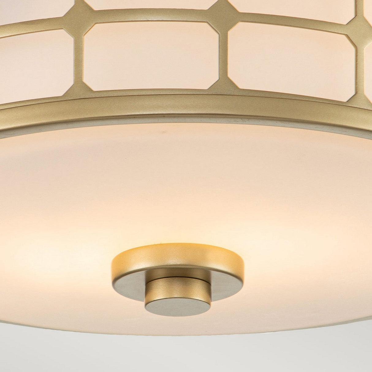 Close-up of the Guardian 2 Light Flush - Painted Natural Brass, perfect for bathroom lighting with its circular design, white cover, and geometric gold pattern along the edge. A small central gold knob is visible at the base, while the natural brass fixture emits a soft, warm glow.