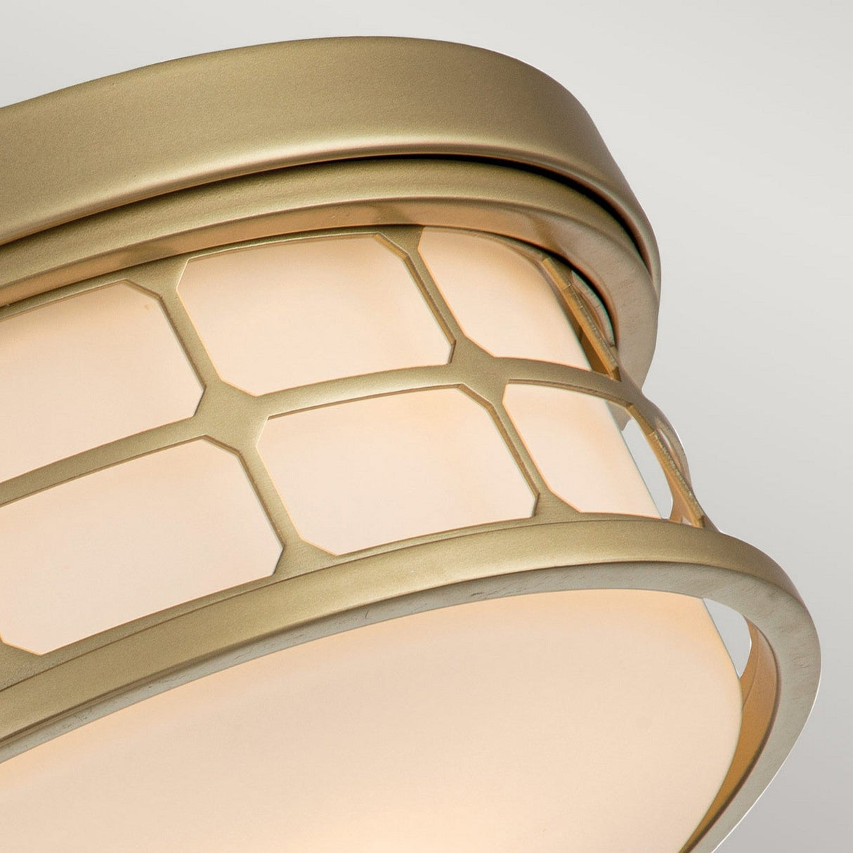 The Guardian 2 Light Flush features a beige ceiling light fixture with a geometric metal cage pattern on the glass. The frame is painted in natural brass, offering an elegant touch that makes it perfect for sophisticated bathroom lighting.