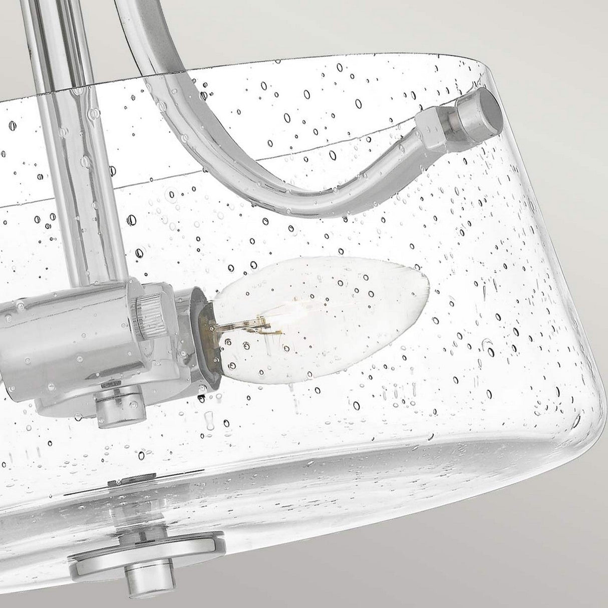 Close-up of a modern ceiling light fixture made of sleek metallic material with a polished nickel finish, showcasing the Hollister 2 Light Semi-Flush design. It features a seeded glass shade with small bubbles, allowing the lightbulb inside to be visible and creating a contemporary look.