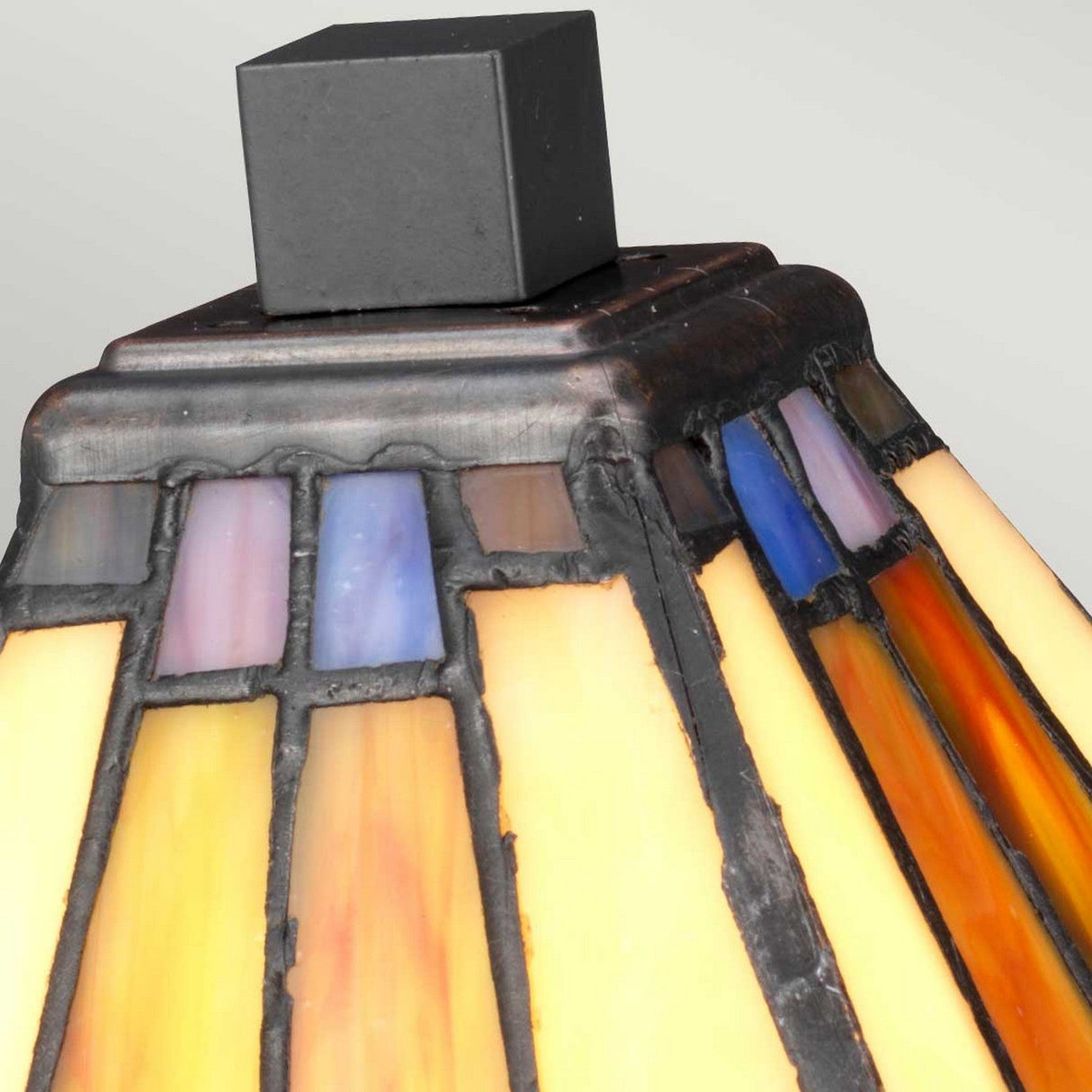 Close-up of the Holmes 1 Light Mini Tiffany Table Lamp, featuring a square black top and a stained glass shade in warm tones of yellow, orange, and blue accents arranged in a geometric pattern, complemented by vintage bronze elements.