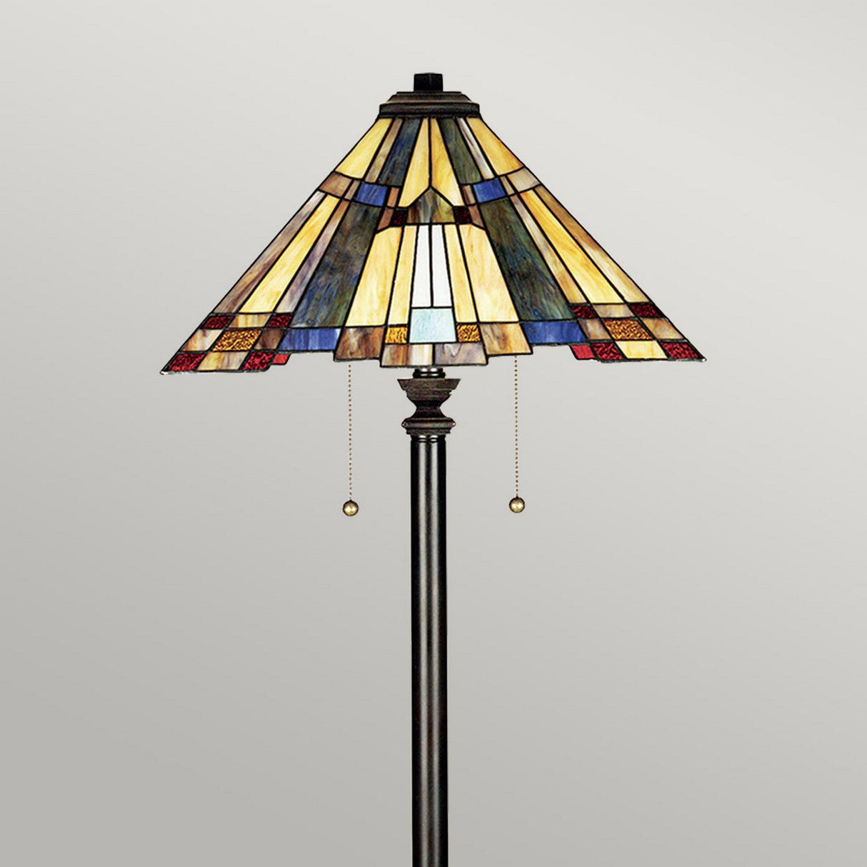 The Inglenook 2 Light Floor Lamp in Valiant Bronze features an art glass shade with a geometric design in shades of yellow, blue, and red. This Arts & Crafts floor lamp also includes two pull chains.