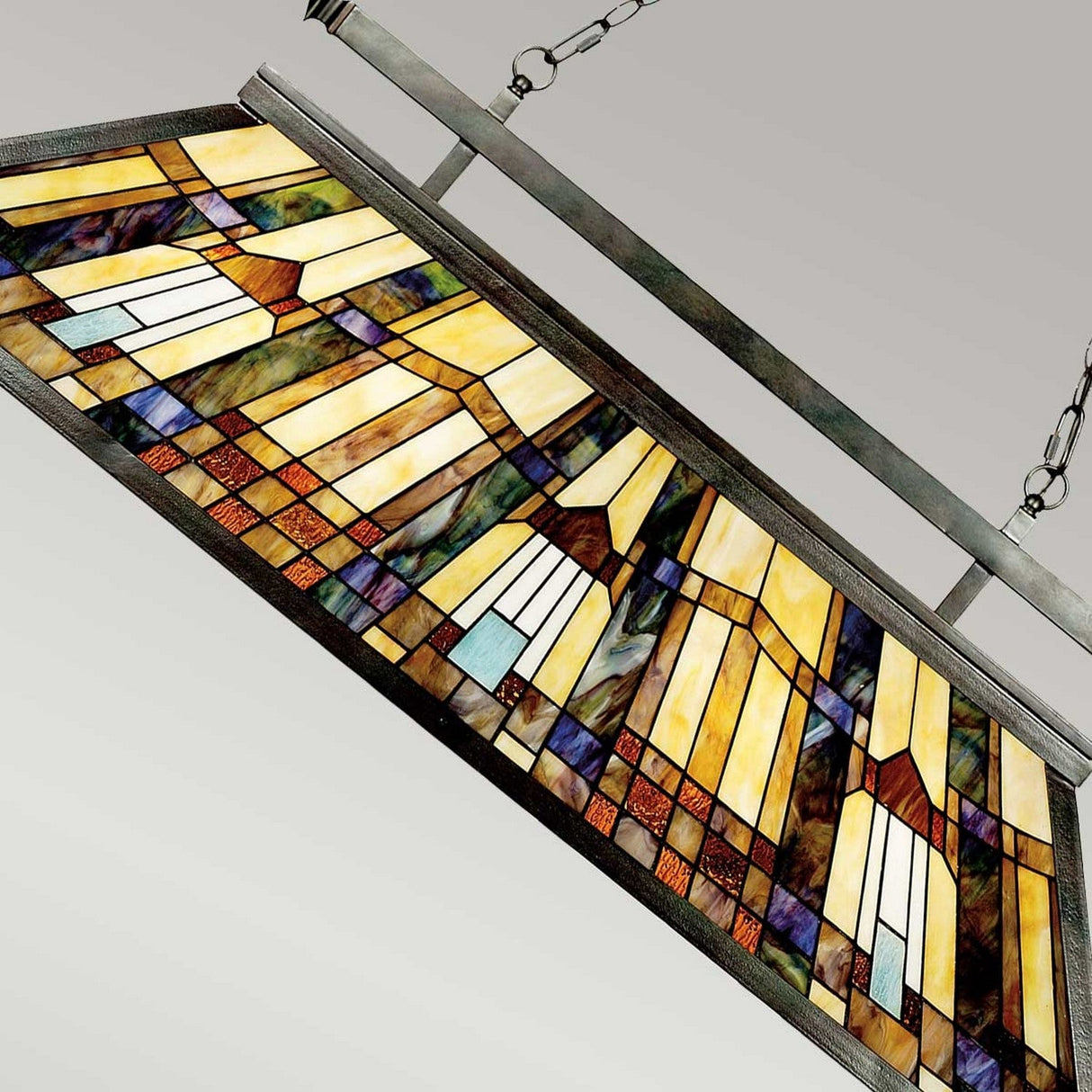 A rectangular stained glass panel featuring geometric patterns in yellow, brown, blue, and green hangs gracefully from metal chains. Its design includes a series of abstractly arranged rectangular sections, exuding the elegance reminiscent of an Inglenook 3 Light Tiffany Island Chandelier in a Valiant Bronze finish.