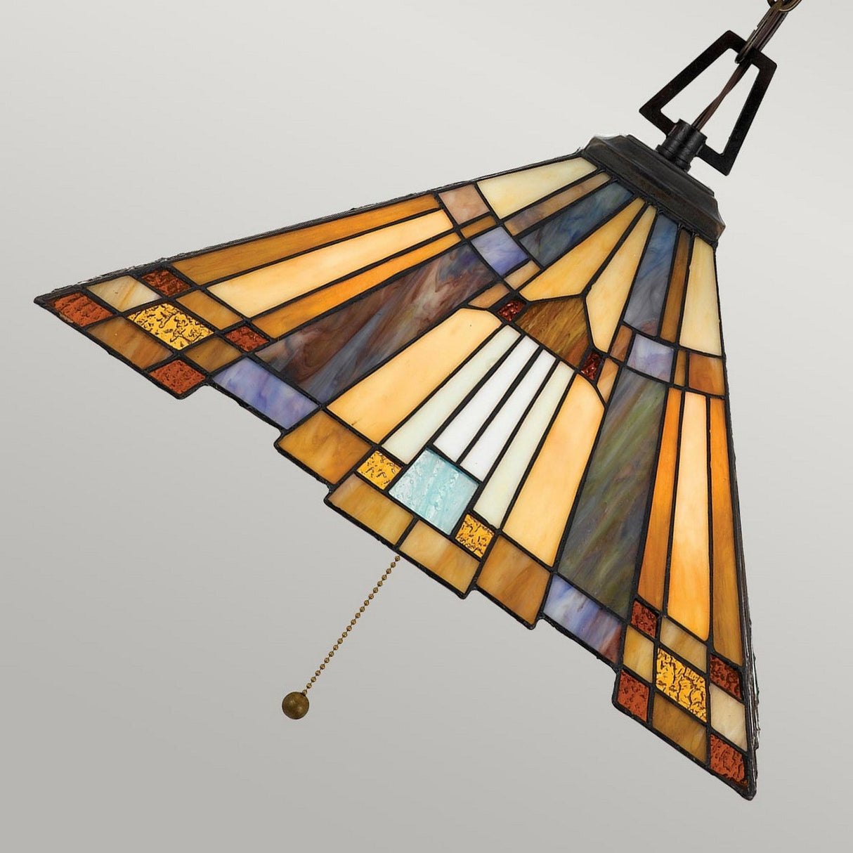 The Inglenook 3 Light Small Tiffany Pendant in Valiant Bronze showcases a stained glass shade adorned with geometric patterns in hues of orange, yellow, blue, and brown. It features a decorative pull chain and hangs with elegance against a light gray backdrop, capturing the essence of the Arts & Crafts style.