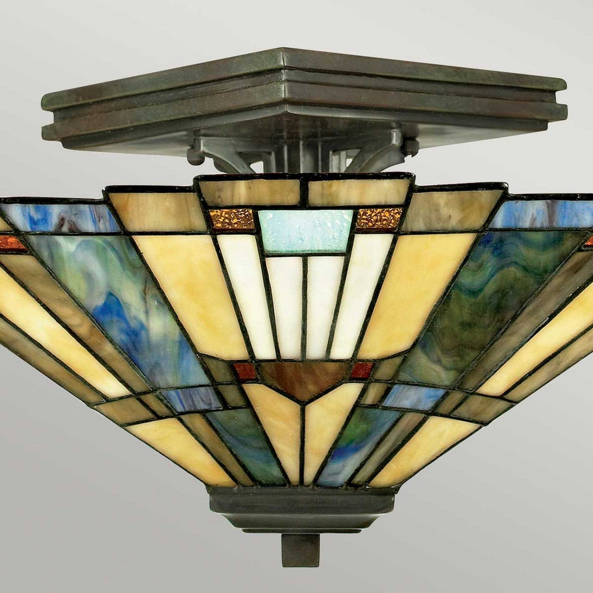 The Inglenook 2 Light Tiffany Semi-Flush - Valiant Bronze features a stained glass shade in a geometric design with shades of yellow, blue, and white, complemented by hints of brown and green. Its square metallic base and art deco-inspired pattern lend an Arts & Crafts flair.