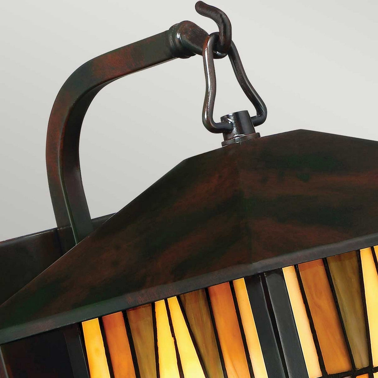 Close-up of the Inglenook Outdoor 1 Light Medium Wall Lantern in Valiant Bronze, showcasing its geometric design. This piece features warm amber and black glass panels in an Arts & Crafts style, complemented by a dark metal frame.