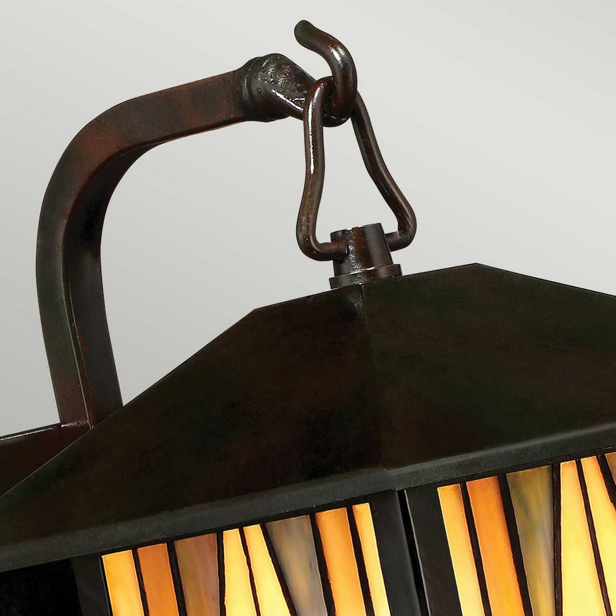 Close-up of the Inglenook Outdoor 1 Light Small Wall Lantern in Valiant Bronze, showcasing an elegant dark metal frame and handle. Its vertical stained glass panels in shades of yellow, orange, and cream evoke an Arts & Crafts style for a warm, vintage appearance.