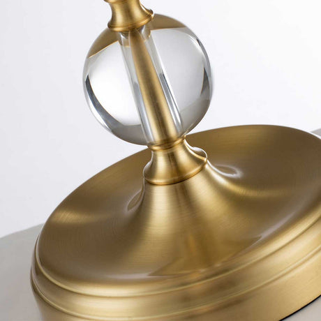 Close-up of the Jenkins 1 Light Table Lamp in brushed brass, showcasing a golden base with a circular pedestal and a decorative transparent glass orb at its center. The metal surface features a reflective, polished finish, epitomizing modern elegance lighting.