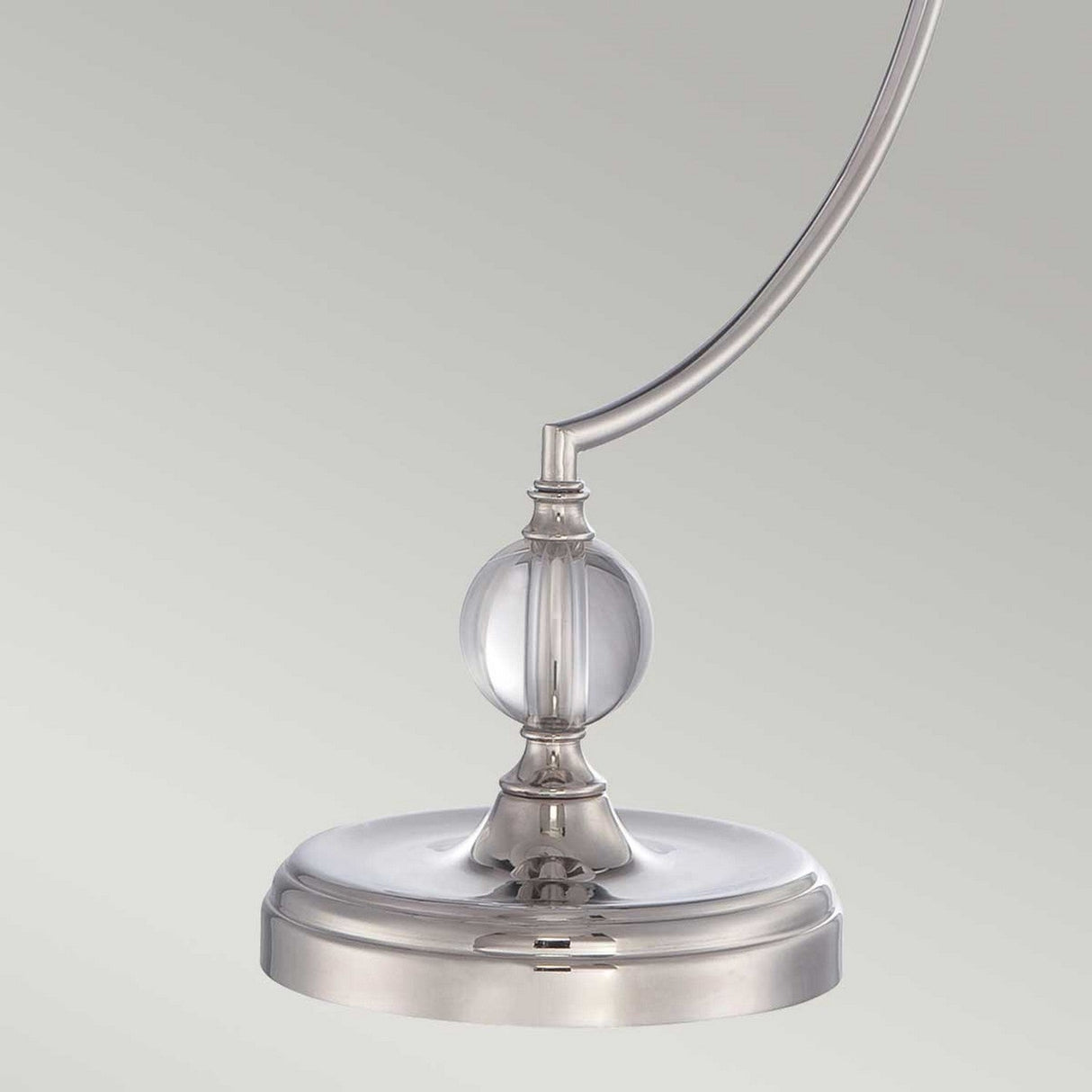 The Jenkins 1 Light Table Lamp features a sleek, modern design with a curved metal stem and a round glass accent at its center, all set against a plain background. This minimalist piece comes in a polished nickel finish, making it an ideal addition to contemporary decor.