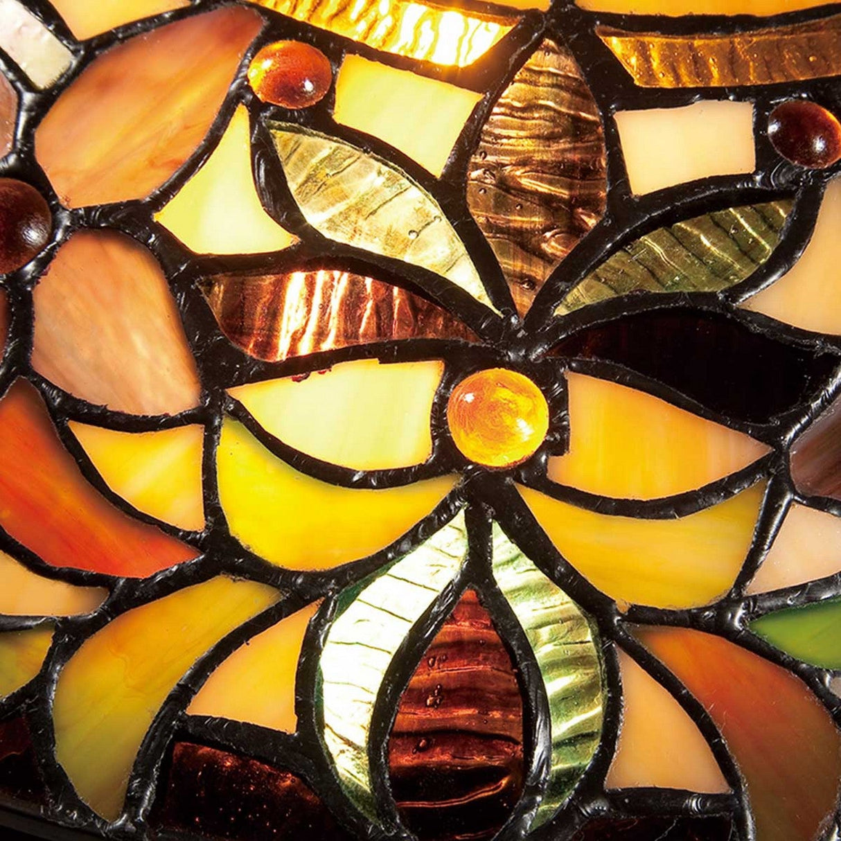 Close-up of the Kami 2 Light Tiffany Flush in a vintage bronze finish, showcasing a stained glass pattern with floral and leaf designs. The warm hues of yellow, orange, red, and green are outlined by black lines, creating a rich mosaic effect that is beautifully illuminated as light passes through.