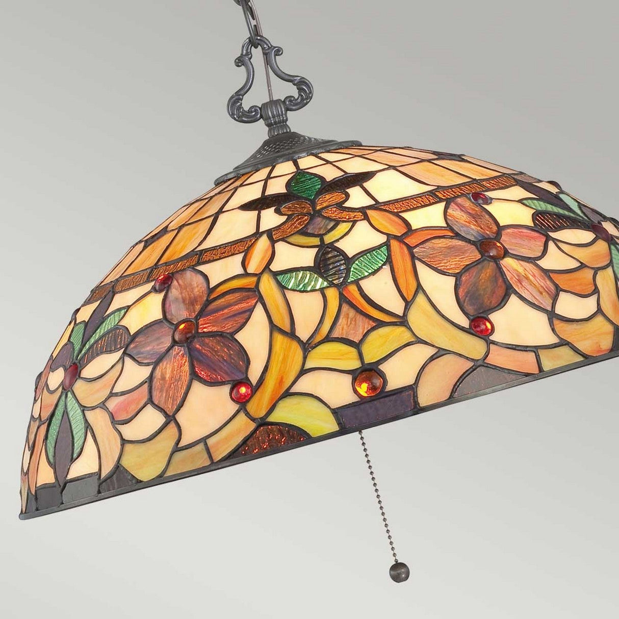 The Kami 3 Light Tiffany Pendant in Vintage Bronze features a stained glass shade showcasing a dome-shaped floral pattern in earthy shades of orange, green, and red. It is accentuated by vintage bronze details and includes a functional pull chain against a light gray background.
