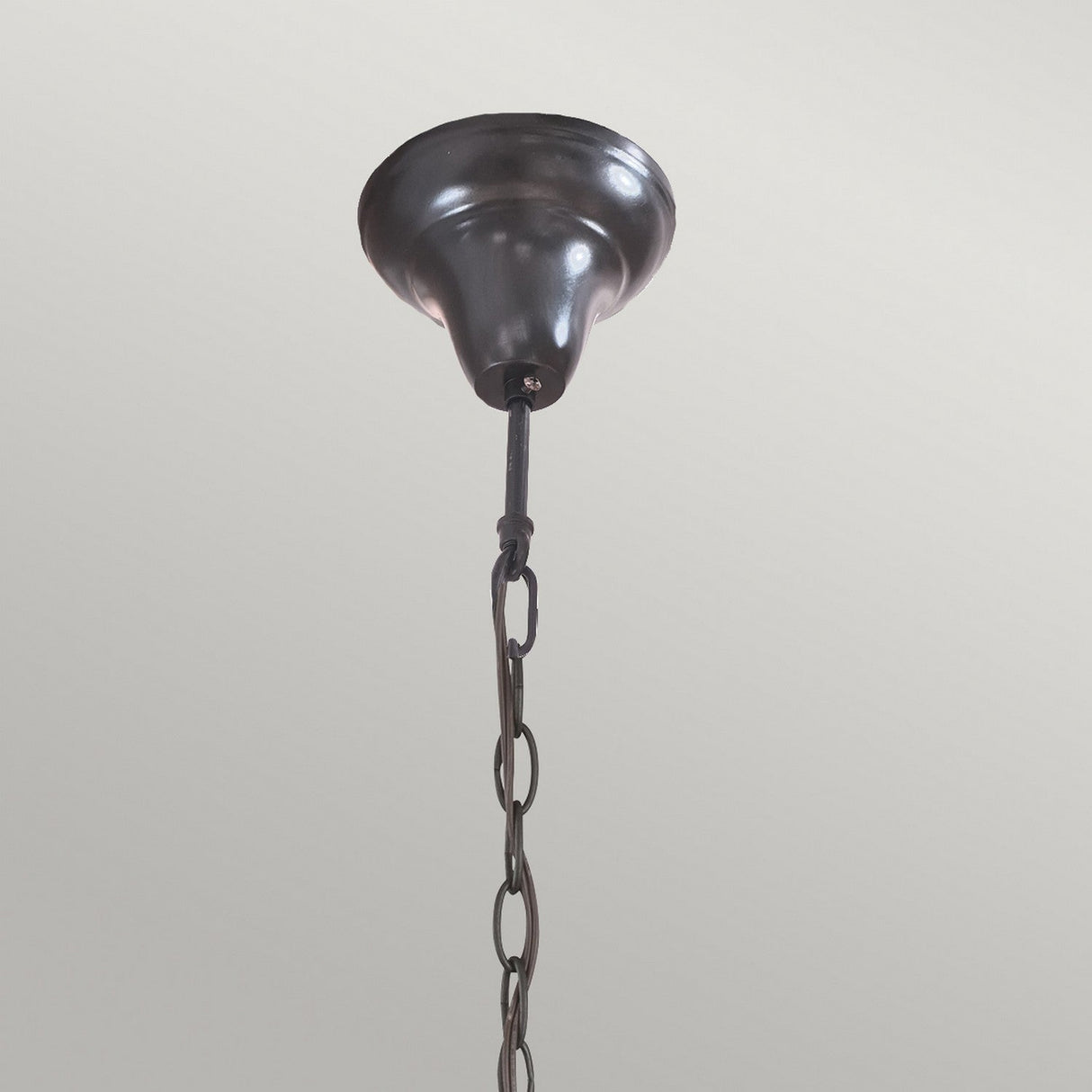 A close-up view showcases the Kami 3 Light Tiffany Pendant in vintage bronze, complete with a chain gracefully extending downward. The simple, light-colored ceiling backdrop perfectly underscores the timeless elegance of this exquisite fixture.