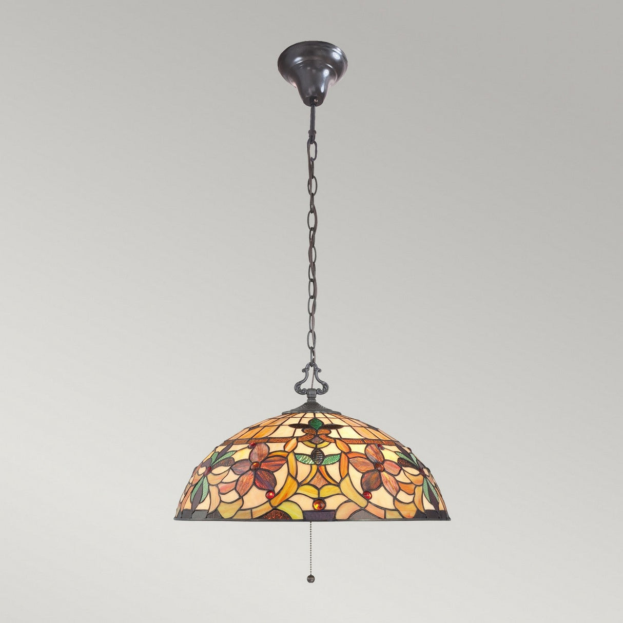 The Kami 3 Light Tiffany Pendant - Vintage Bronze, featuring a stained glass shade with a floral pattern, hangs from a chain. Its dome-shaped design showcases rich earthy tones of orange, yellow, and green that cast a warm glow imbued with vintage bronze charm.