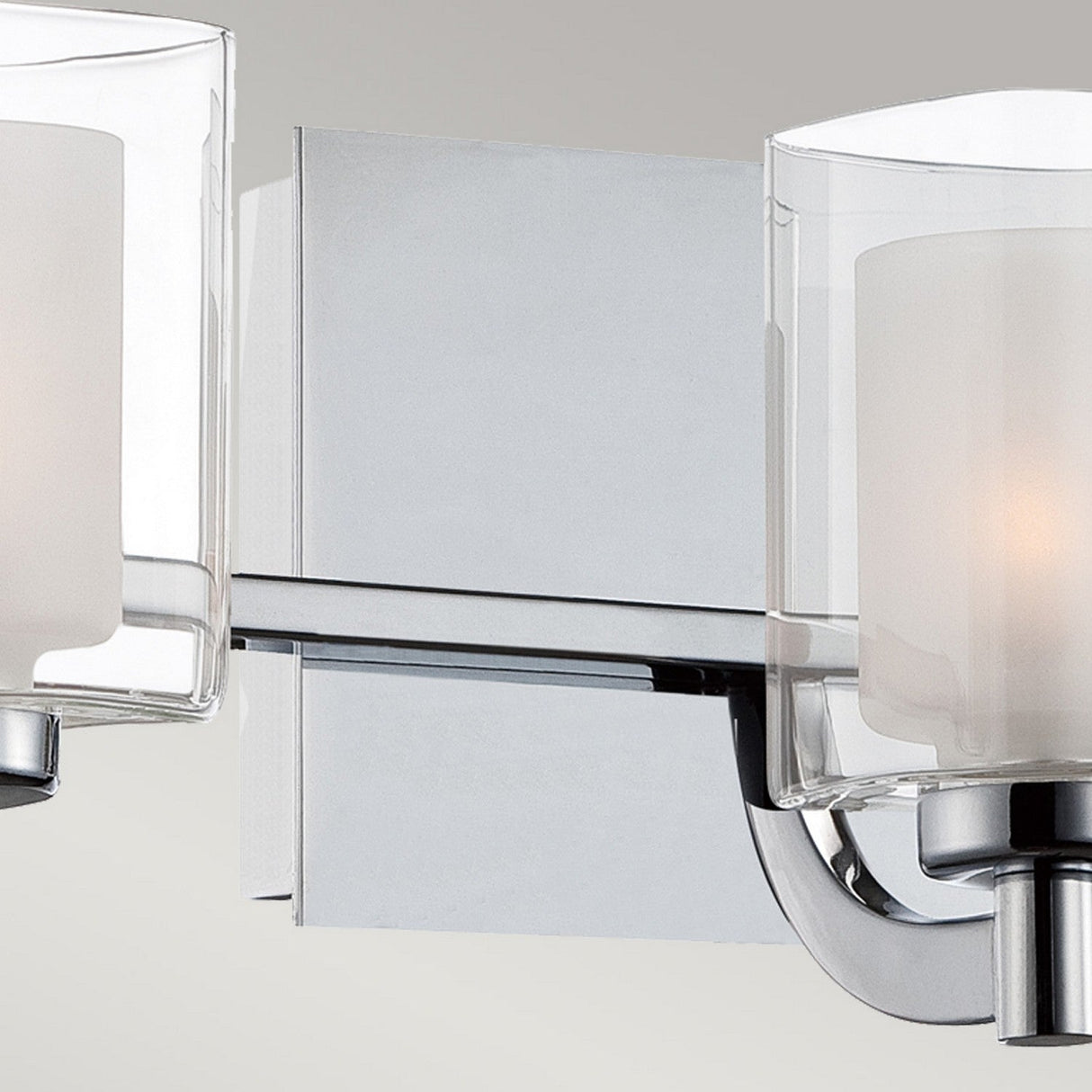 Close-up of the Kolt 3 Light Semi-Flush - Polished Chrome, a contemporary wall-mounted bathroom lighting fixture with a polished chrome base and two frosted glass shades encased in clear glass cylinders, providing a soft glow.
