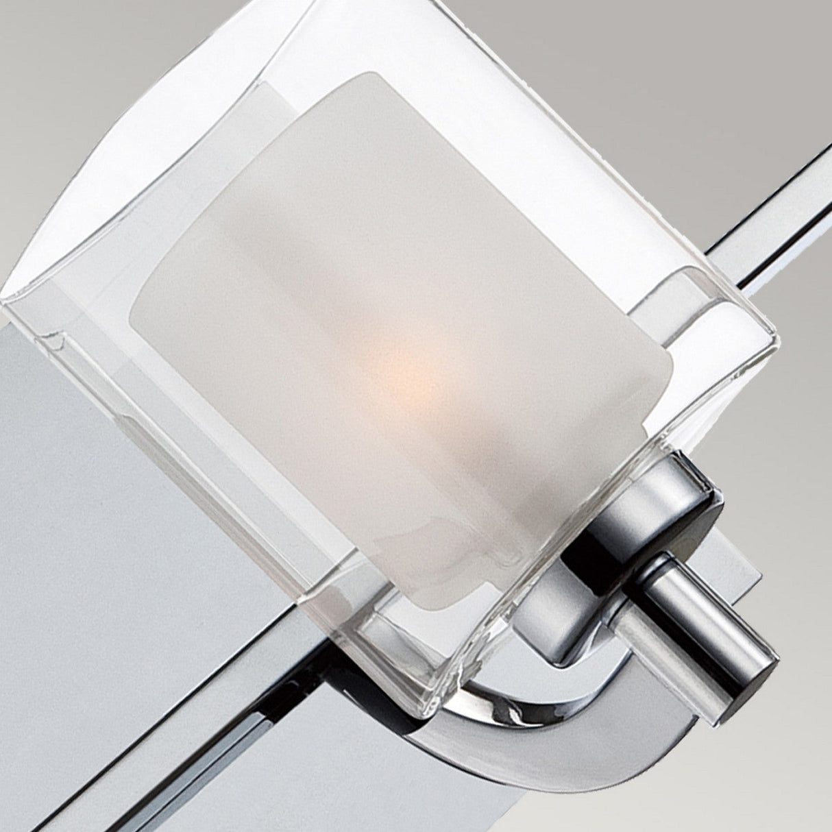 A close-up view of the Kolt 3 Light Semi-Flush in polished chrome showcases its contemporary wall sconce design. It features a frosted glass shade enclosed within a transparent rectangular frame, mounted on a smooth metallic base that embodies minimalist elegance—ideal for bathroom lighting.