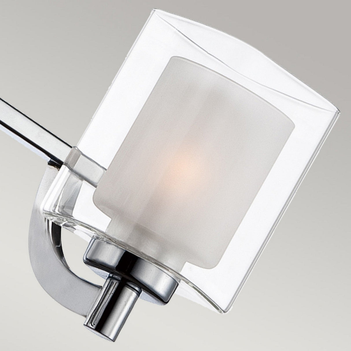 Close-up of the Kolt 3 Light Semi-Flush in polished chrome, featuring a modern wall light fixture with a square glass shade. The design includes a frosted inner cylinder and polished chrome arm, casting a warm glow. Ideal for bathroom lighting, this piece adds elegance while maintaining its functional charm.