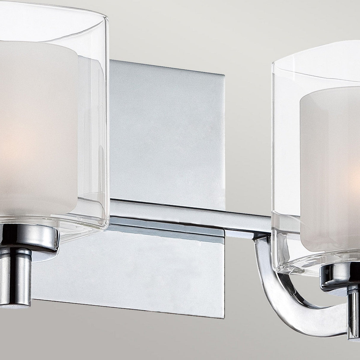 Introducing the Kolt 2 Light Wall Light in Polished Chrome—a contemporary, wall-mounted fixture featuring dual-layer glass shades that encase glowing bulbs. Ideal for bathroom lighting, its polished chrome finish is complemented by elegant curved metal arms supporting the shades, all set against a plain and neutral background.