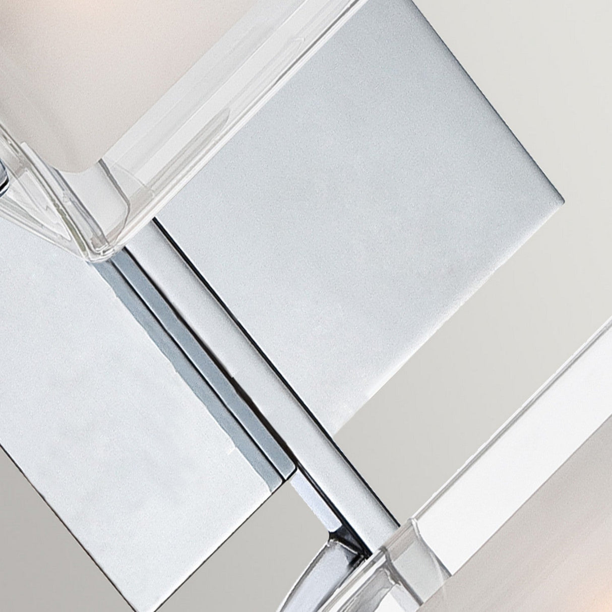 Discover the Kolt 2 Light Wall Light in Polished Chrome, showcasing a minimalist abstract design with interlocking clear and metallic geometric shapes. Its mirrored surfaces and dual-layer glass elements, combined with polished chrome accents, create a sleek and modern aesthetic ideal for sophisticated bathroom lighting.