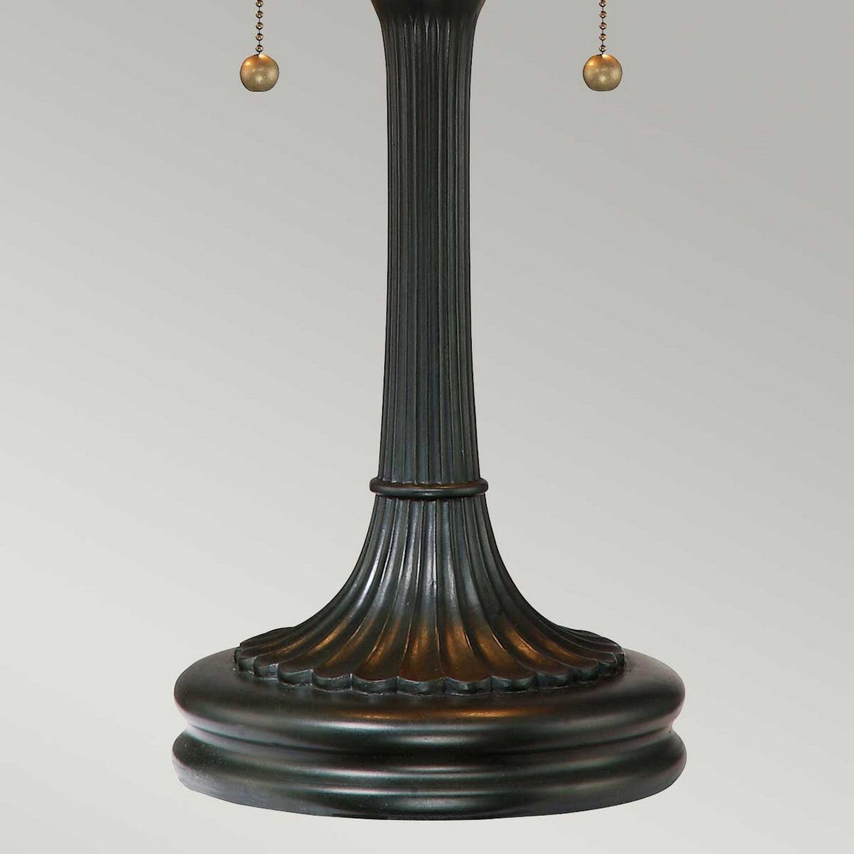 The Larissa 2 Light Tiffany Table Lamp in Vintage Bronze features a classic fluted column design, complete with two hanging pull chains that capture the essence of Tiffany charm. Its slightly worn patina enhances its timeless appeal, while the neutral gray background complements its elegant style.