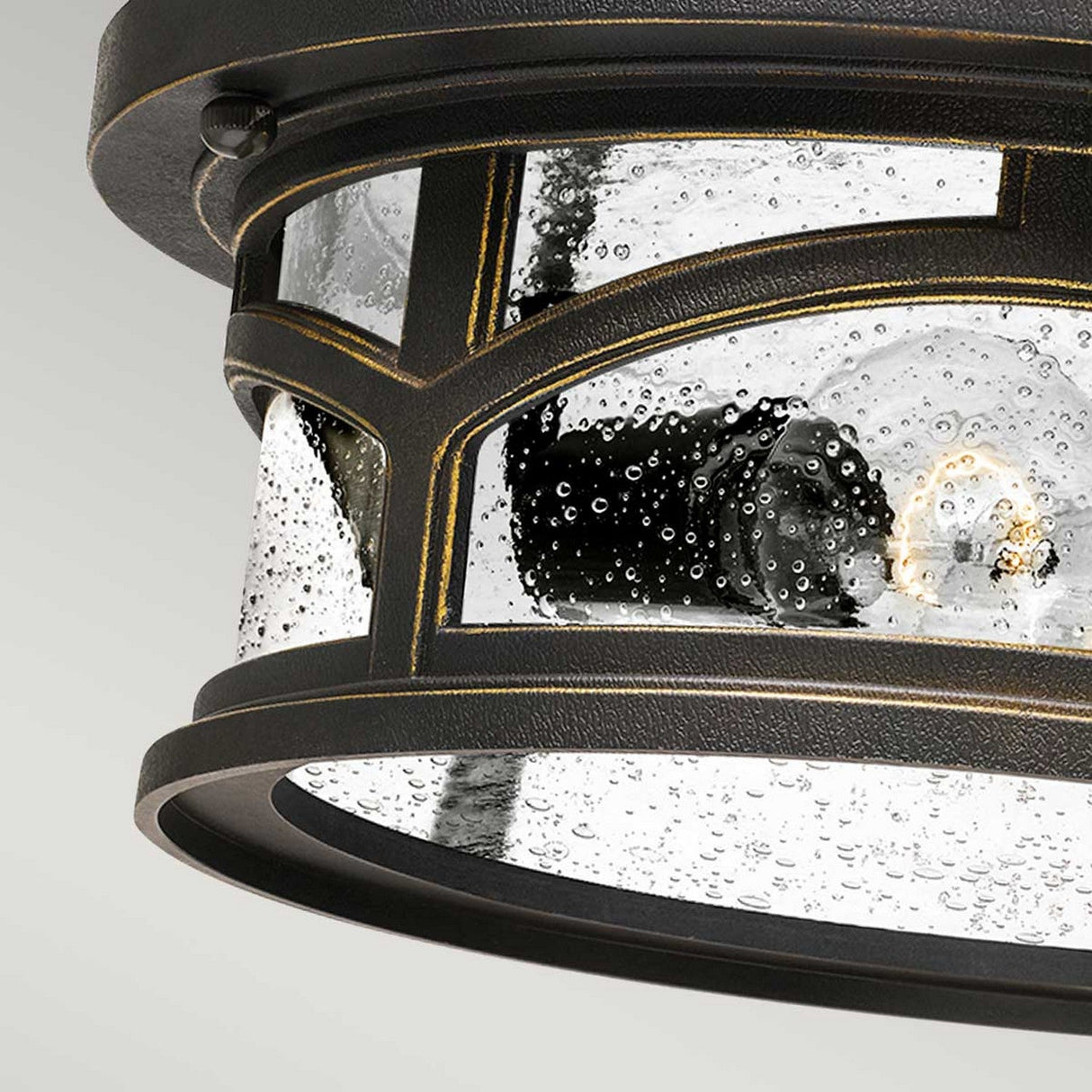 Close-up of the Marblehead Outdoor 2 Light Flush in Palladian Bronze, featuring a weather-resistant, round ceiling light fixture with a black metal frame and clear bubbled glass panels. Its textured glass and Palladian Bronze accents enhance its elegance, while the visible bulb inside emits a soft glow.
