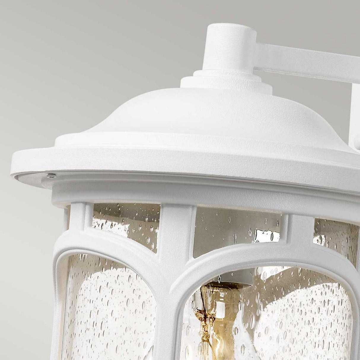 A detailed view of the Marblehead Outdoor 1 Light Medium Wall Lantern in white, showcasing its clear seedy glass panels. The design includes elegantly curved metal accents, while the bulb inside emits a cozy glow. Its weather-resistant construction makes it stand out against the light, neutral background.