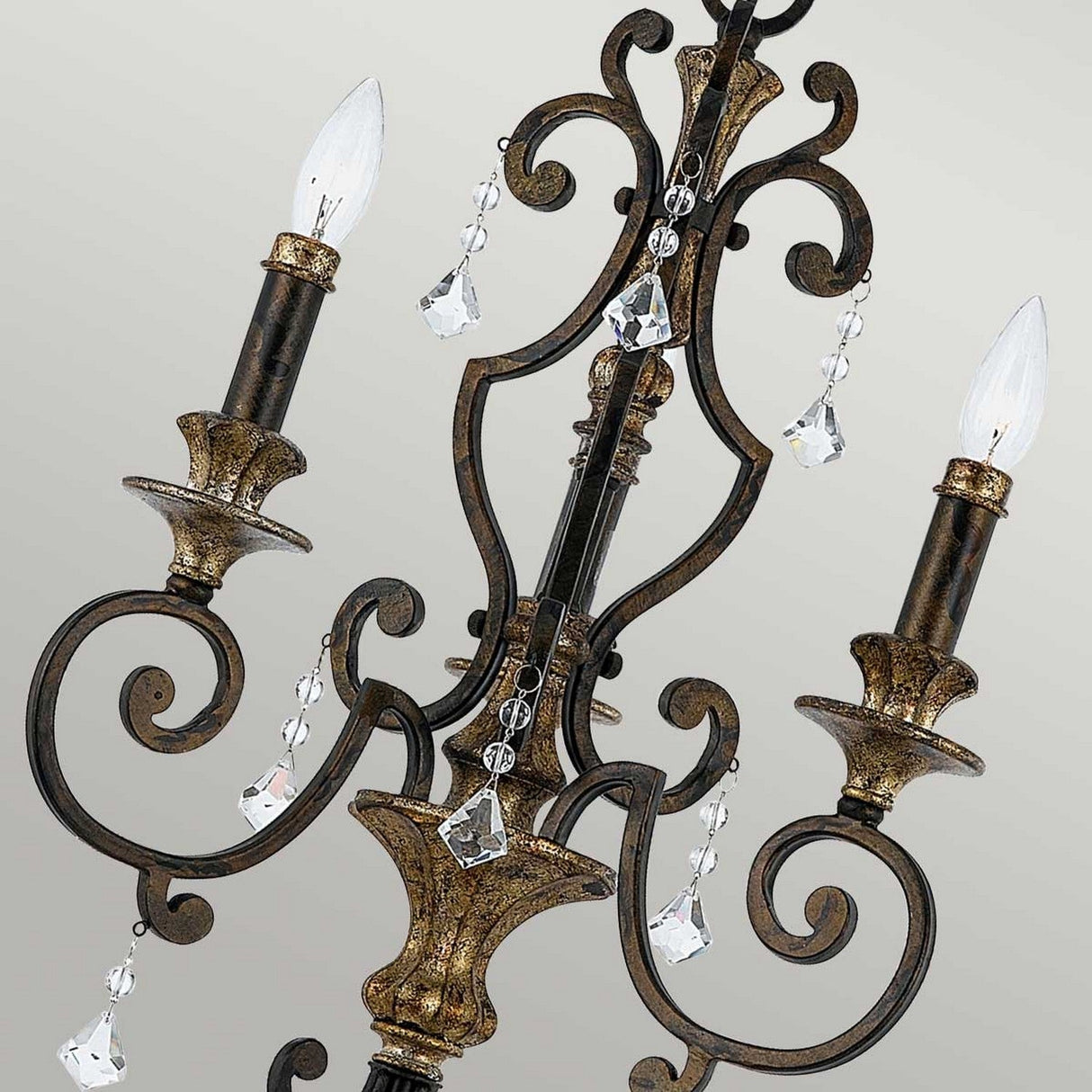 The Marquette 3 Light Chandelier - Bronze features an intricate, vintage-style design with three candle-shaped lights. Its black and gold metal framework, adorned with hanging crystal drops, showcases an elegant and classic aesthetic enhanced by a bronze finish.