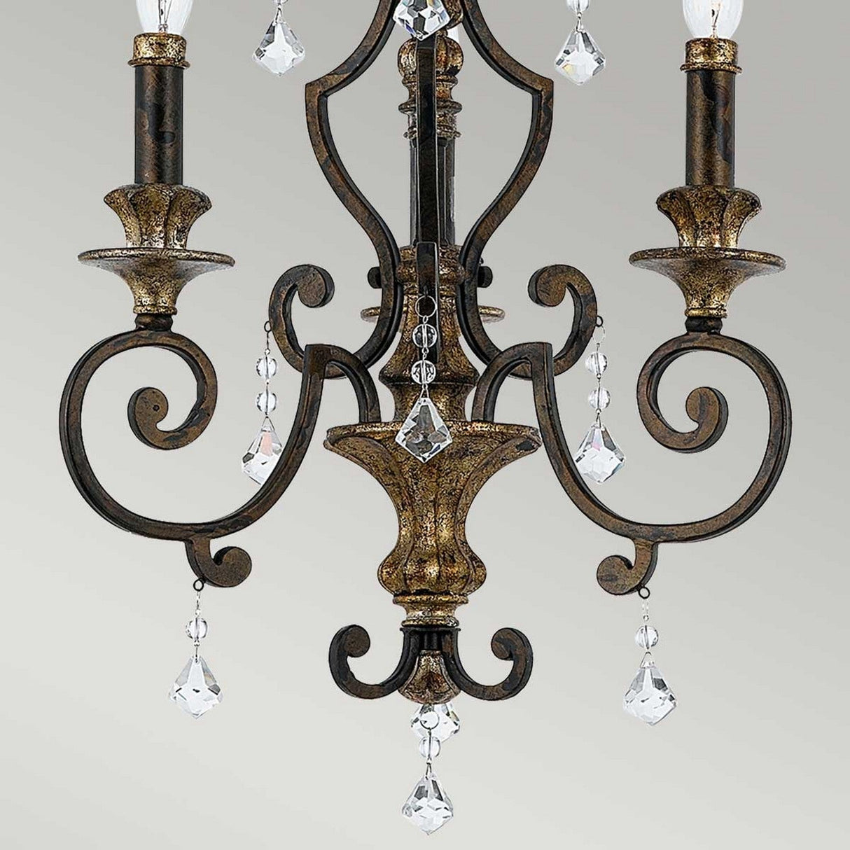 The Marquette 3 Light Chandelier in bronze showcases a breathtaking antique finish with exquisite scrollwork and faceted crystal drops adorning each arm, highlighting its sophisticated design.