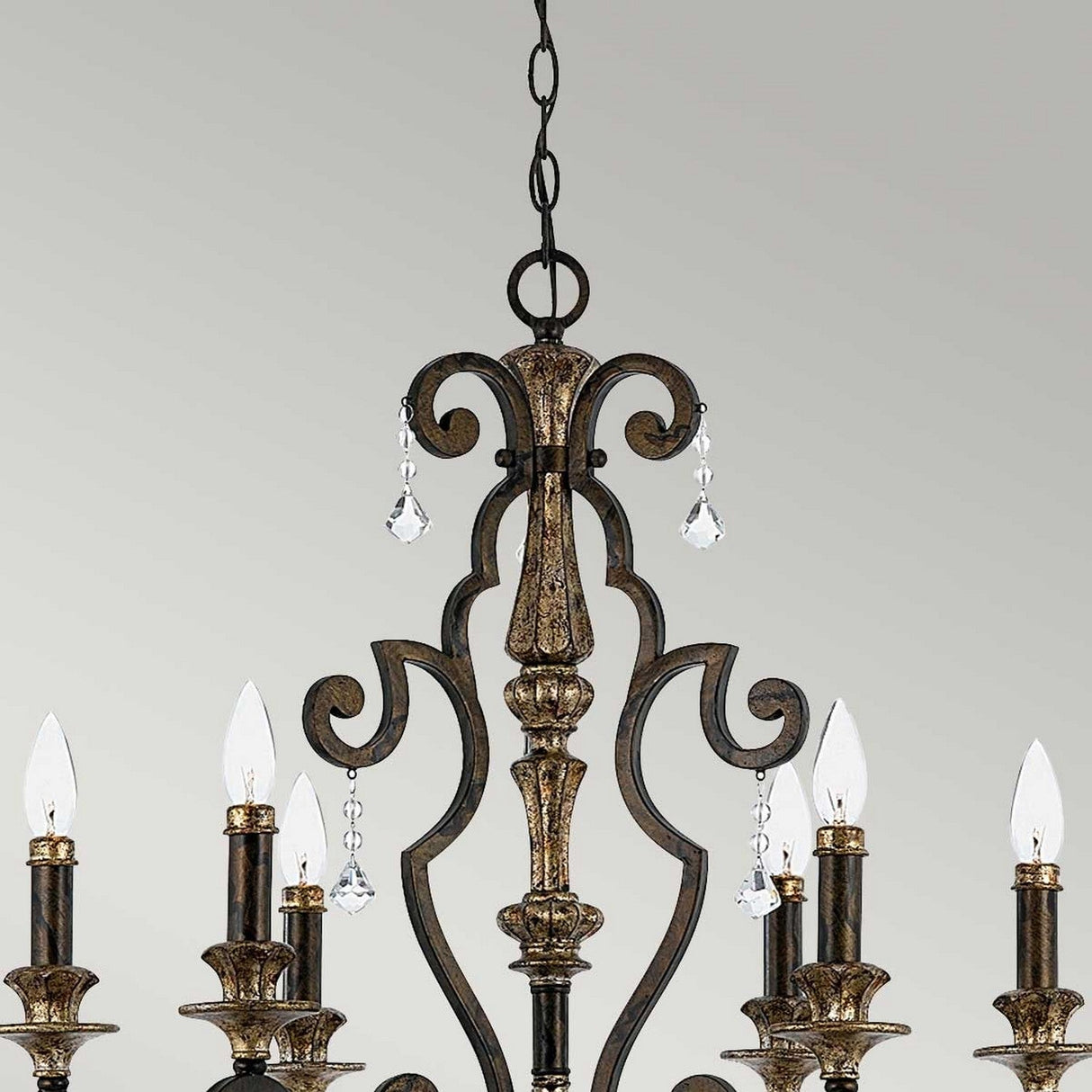 The Marquette-A 6 Light Chandelier - Bronze showcases intricate metalwork and candle-like lights, embellished with sparkling crystal drops, all set against a neutral background.