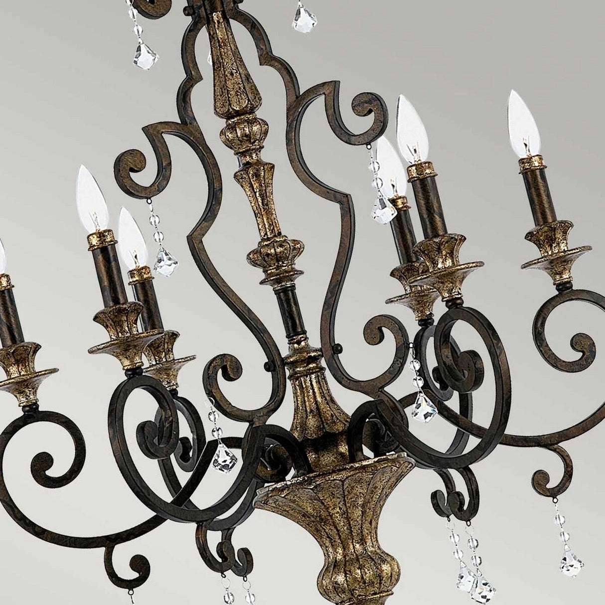 A detailed view of the Marquette-A 6 Light Chandelier - Bronze, showcasing its vintage-style ornate design with dark bronze curving arms and intricate detailing. It features six candle-like lights and is adorned with small crystal drops, set against a plain background.