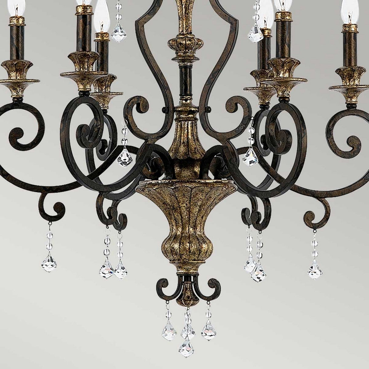Discover the elegance of the Marquette-A 6 Light Chandelier - Bronze. This vintage-inspired chandelier showcases intricate bronze metal scrollwork and an ornate central column, adorned with multiple candle-shaped lights. It features shimmering crystal drops and hanging glass pendants, all set against a soft gray background for a timeless look.