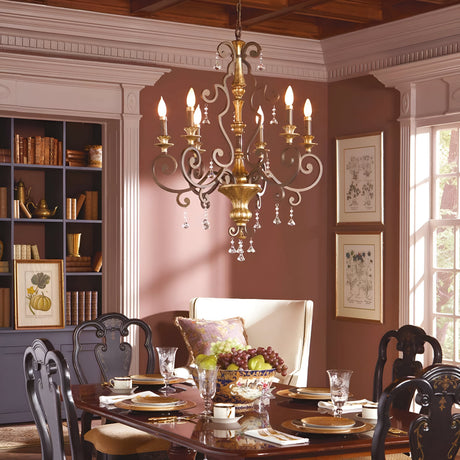 A dining room featuring the sophisticated Marquette-A 6 Light Chandelier in bronze, adorned with crystal drops. Below it is a polished wooden table set for six, complete with plates, glassware, and a fruit bowl. The room also showcases dark wood chairs, a bookshelf, framed artwork, and a large window that lets in natural light.