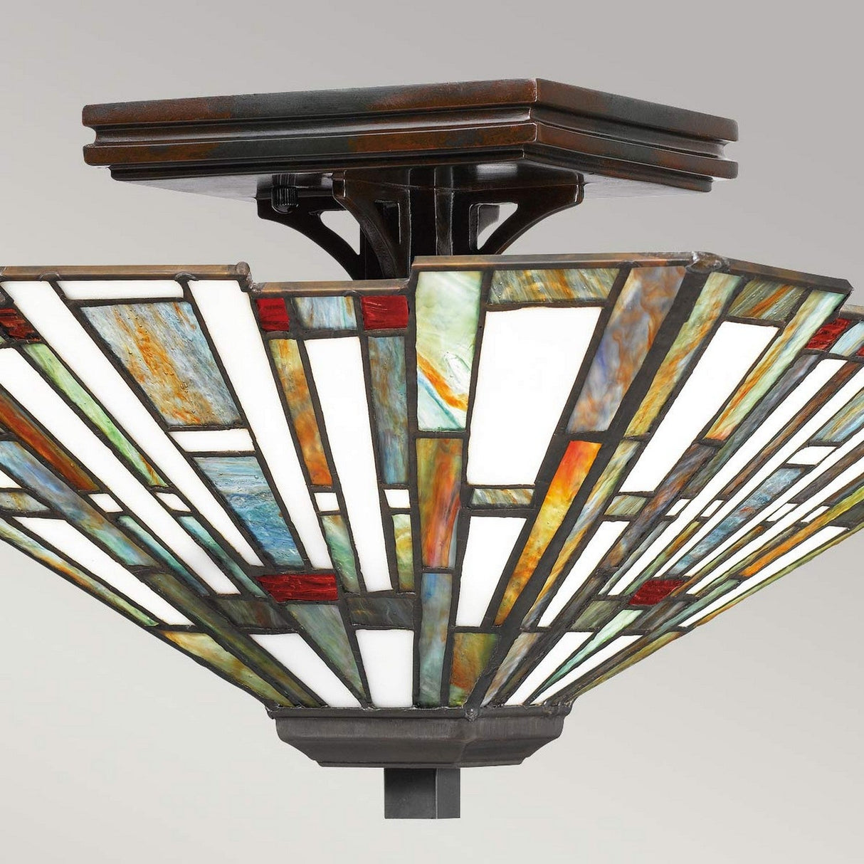 The Maybeck 2 Light Tiffany Flush in Valiant Bronze features a square stained glass fixture with a geometric design in vibrant green, red, and white panels. Its dark metal base complements the handcrafted artistry of the piece, beautifully showcased against a neutral background.
