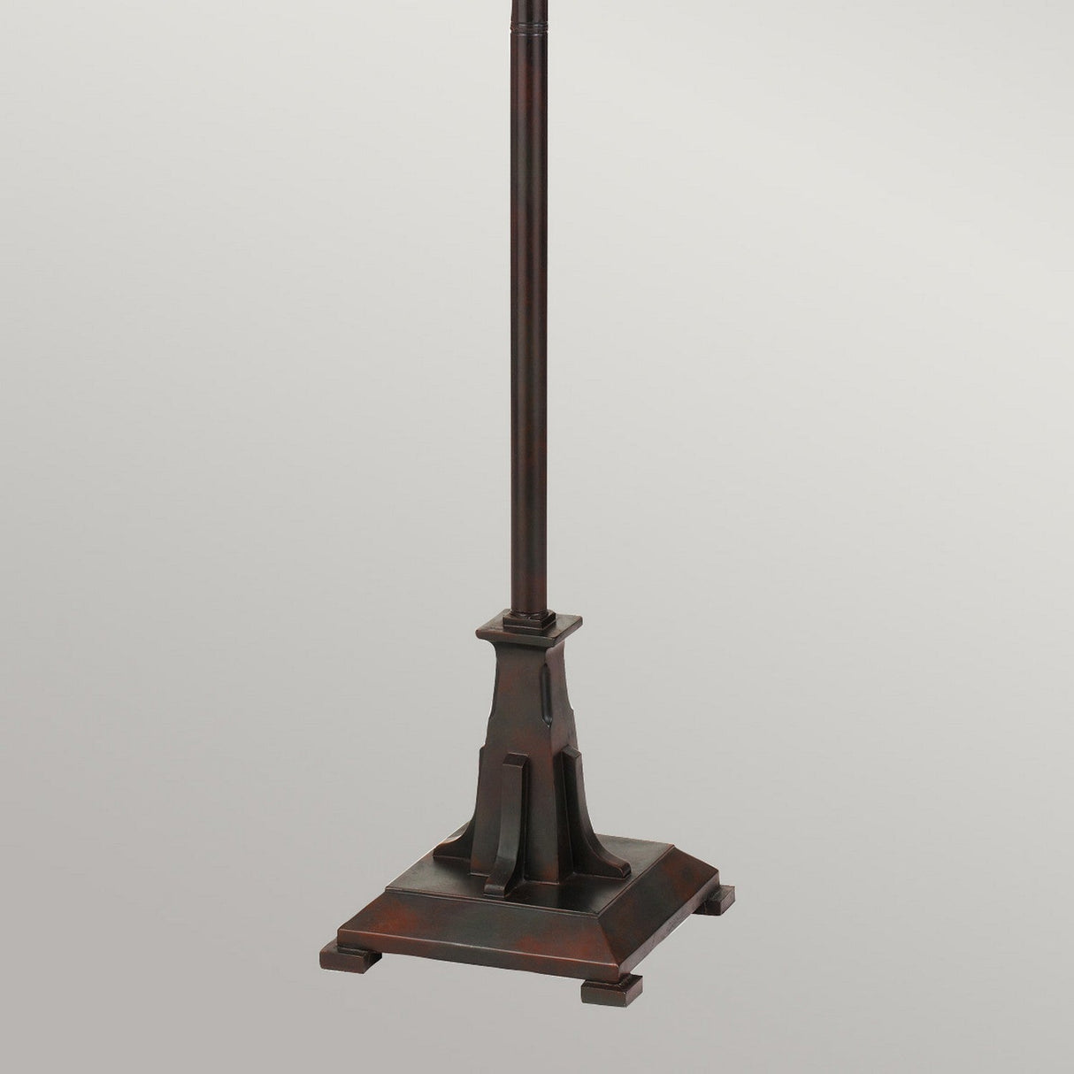 Introducing the Maybeck 2 Light Tiffany Floor Lamp - Valiant Bronze: a beautifully dark bronze-colored base with a square, tiered platform and a tall, slender central column adorned with geometric accents. It stands elegantly against a simple, light gray background.