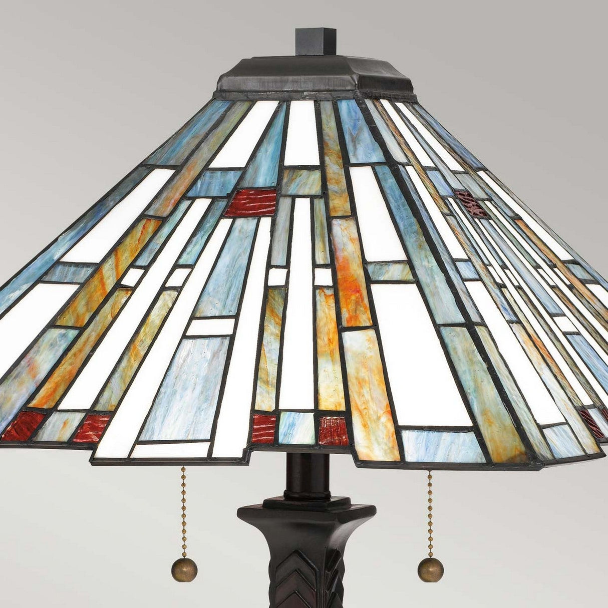 The Maybeck 2 Light Tiffany Table Lamp, featuring a geometric design with handcrafted glass panels in white, blue, orange, and red, includes a valiant bronze base and is equipped with two pull chains for easy operation.