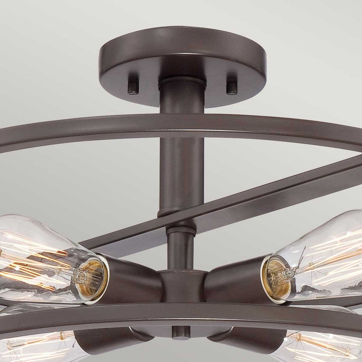 A detailed view of the New Harbor 4 Light Semi-Flush in Western Bronze reveals four Victorian Edison-style bulbs with visible filaments, all encased in a circular metal frame that highlights its rich, industrial appeal.