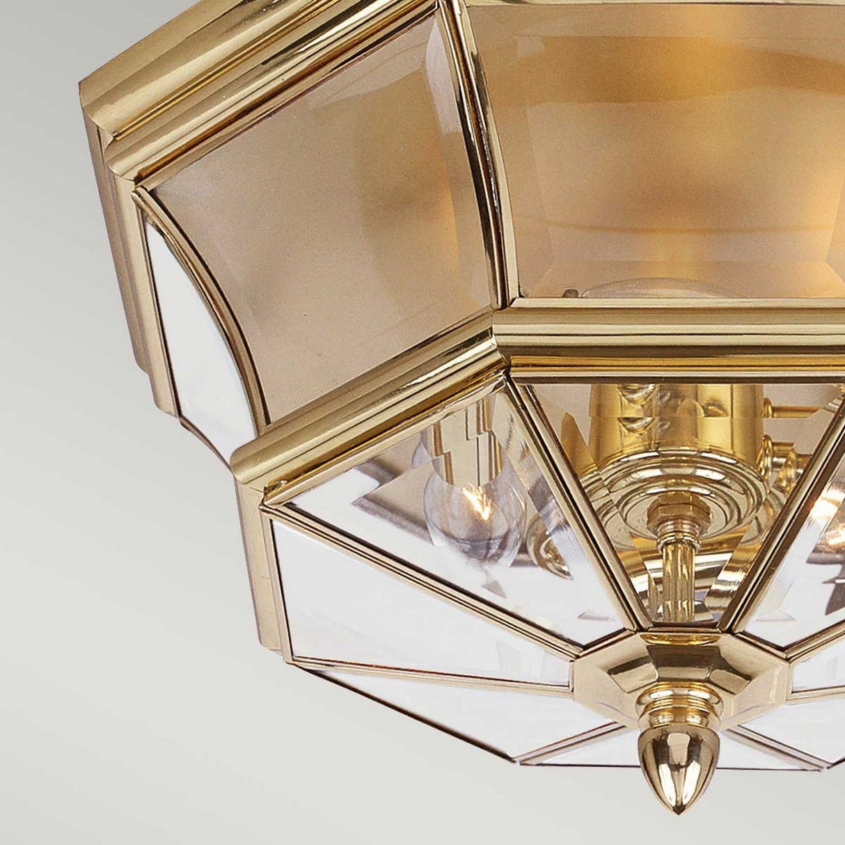 Close-up of the Newbury Outdoor 3 Light Flush in lacquered polished brass, featuring an octagonal design with clear glass panels and visible bulbs. This flush-mount fixture exudes a classic and elegant look against a plain light-colored background.