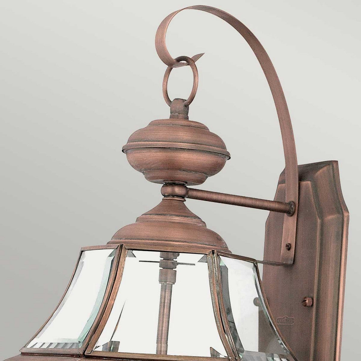 Close-up of the Newbury Outdoor 2 Light Large Wall Lantern with clear beveled glass panels and a curved arm connecting to a wall mount. This lantern, featuring a lacquered aged copper finish, showcases a classic design with a loop finial on top, set against a plain background.