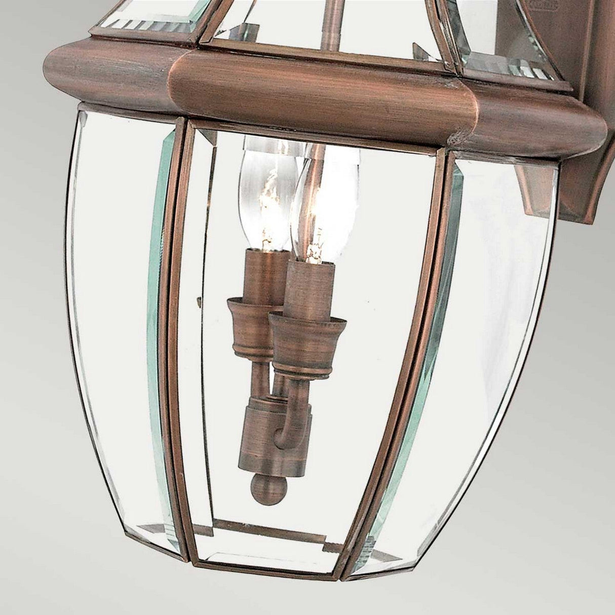 Close-up of the Newbury Outdoor 2 Light Large Wall Lantern, featuring a lacquered aged copper finish and clear beveled glass panes. The lantern displays two candle-like light bulbs inside, elegantly highlighting its classic design.