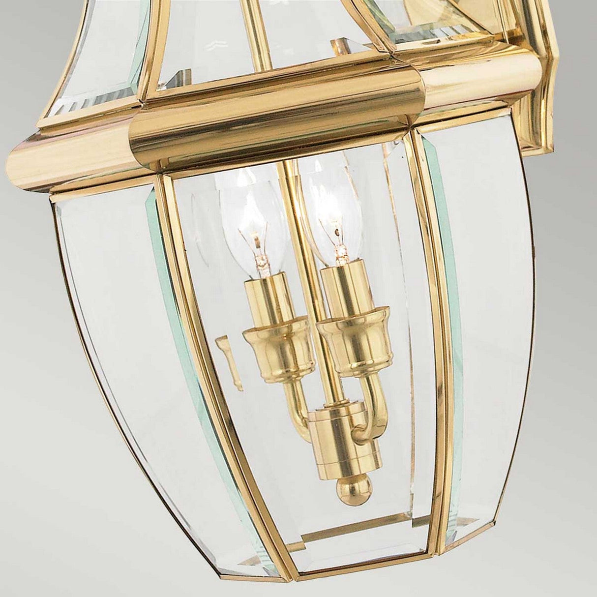 Close-up of the Newbury Outdoor 2 Light Large Wall Lantern in lacquered polished brass, showcasing its lantern-style design with two exposed bulbs. The fixture features clear beveled glass panels and elegant metal framing, embodying a traditional aesthetic.