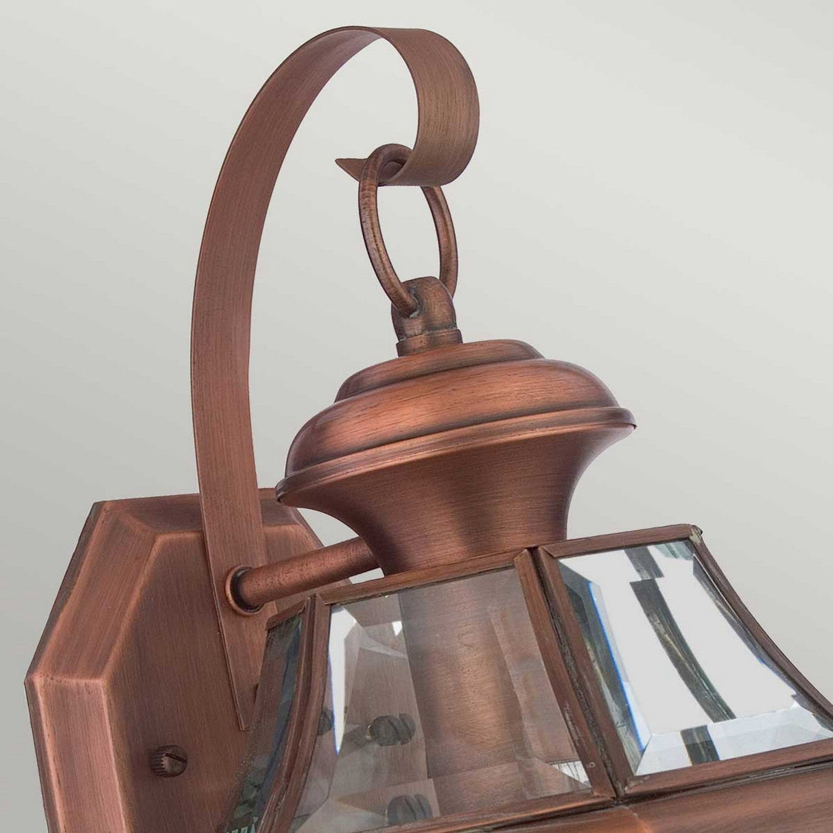 A close-up of the Newbury Outdoor 1 Light Medium Wall Lantern in lacquered aged copper, featuring a rustic and elegant design with a curved arm and clear beveled glass panels, perfect for exterior lighting. The background is a simple, light grey color.