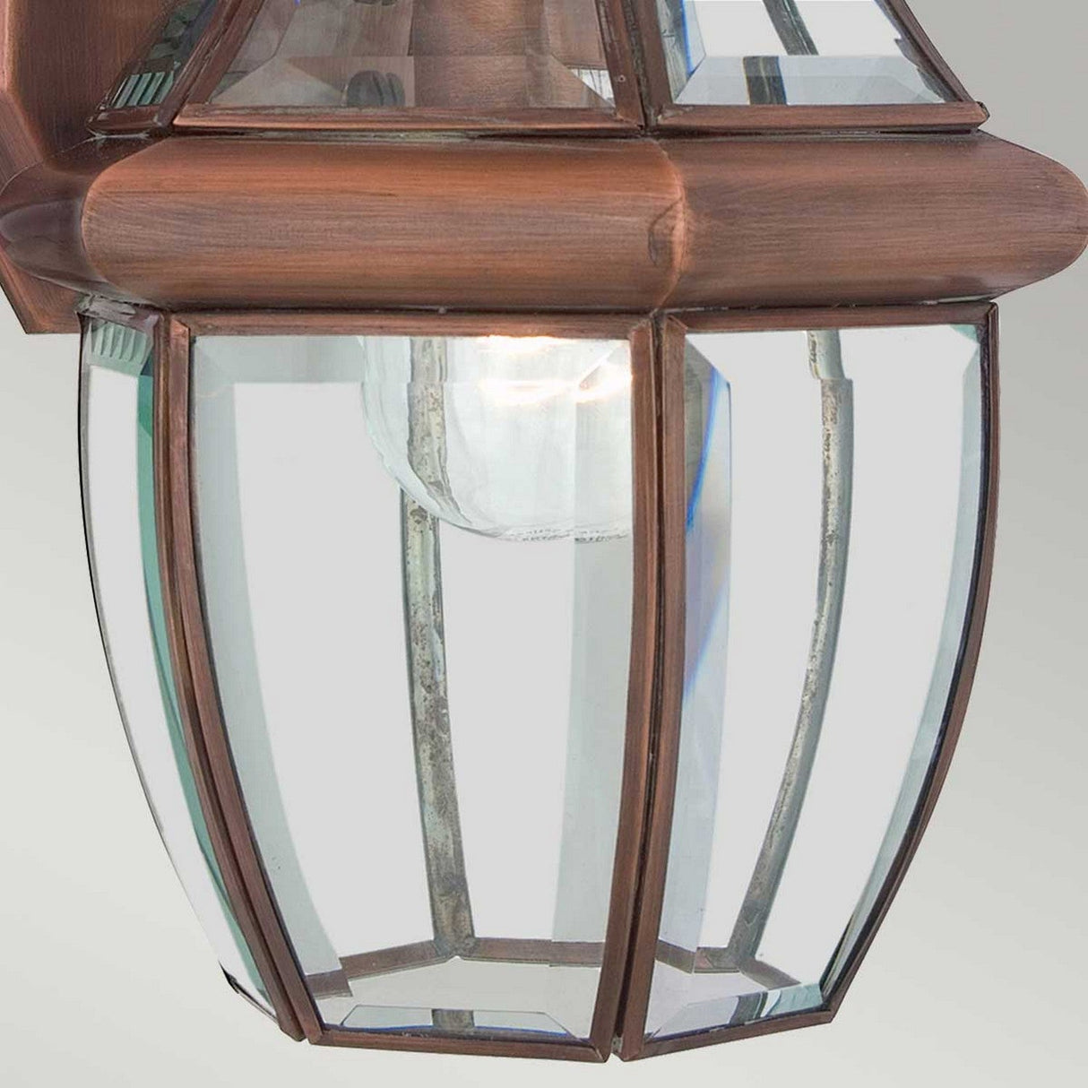 A close-up of the Newbury Outdoor 1 Light Medium Wall Lantern reveals its elegant design with clear beveled glass panels and a lacquered aged copper frame, showcasing a visible light bulb that emits a warm, traditional glow.
