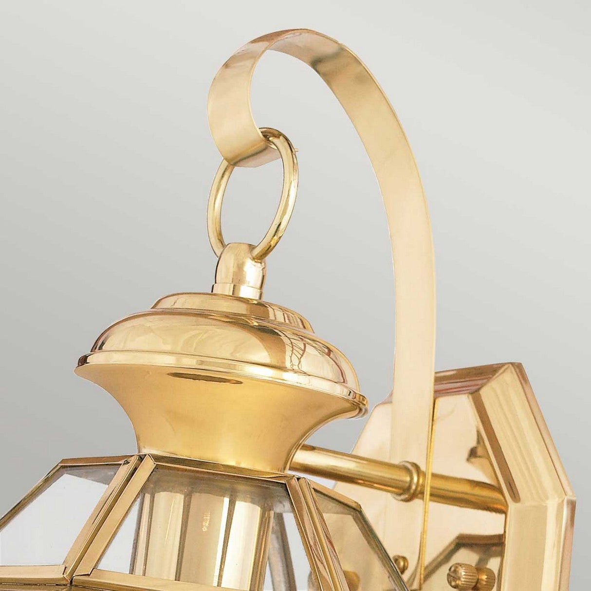 Close-up of the Newbury Outdoor 1 Light Small Wall Lantern in lacquered polished brass, showcasing its curved top handle, sleek beveled glass panels, and classic design against a plain, neutral background.