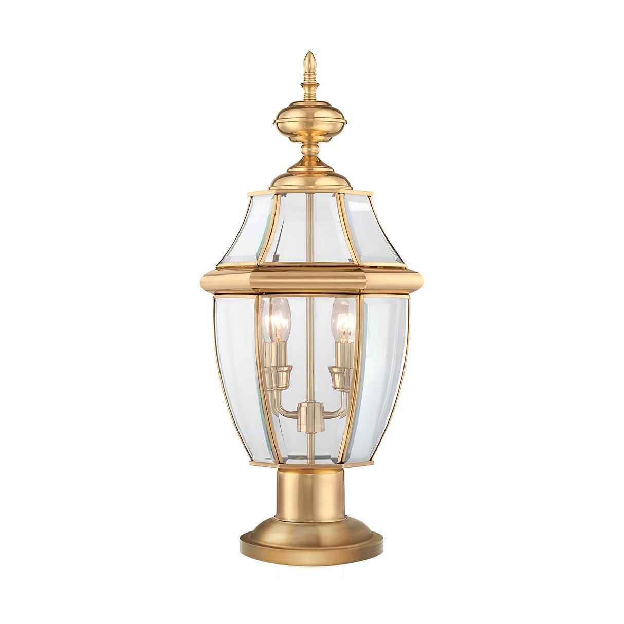The Newbury 2 Light Pedestal in lacquered polished brass, with its two candle-style light bulbs enclosed by clear glass panels and topped with a decorative finial, stands out elegantly as an outdoor lighting centerpiece against a plain white background.