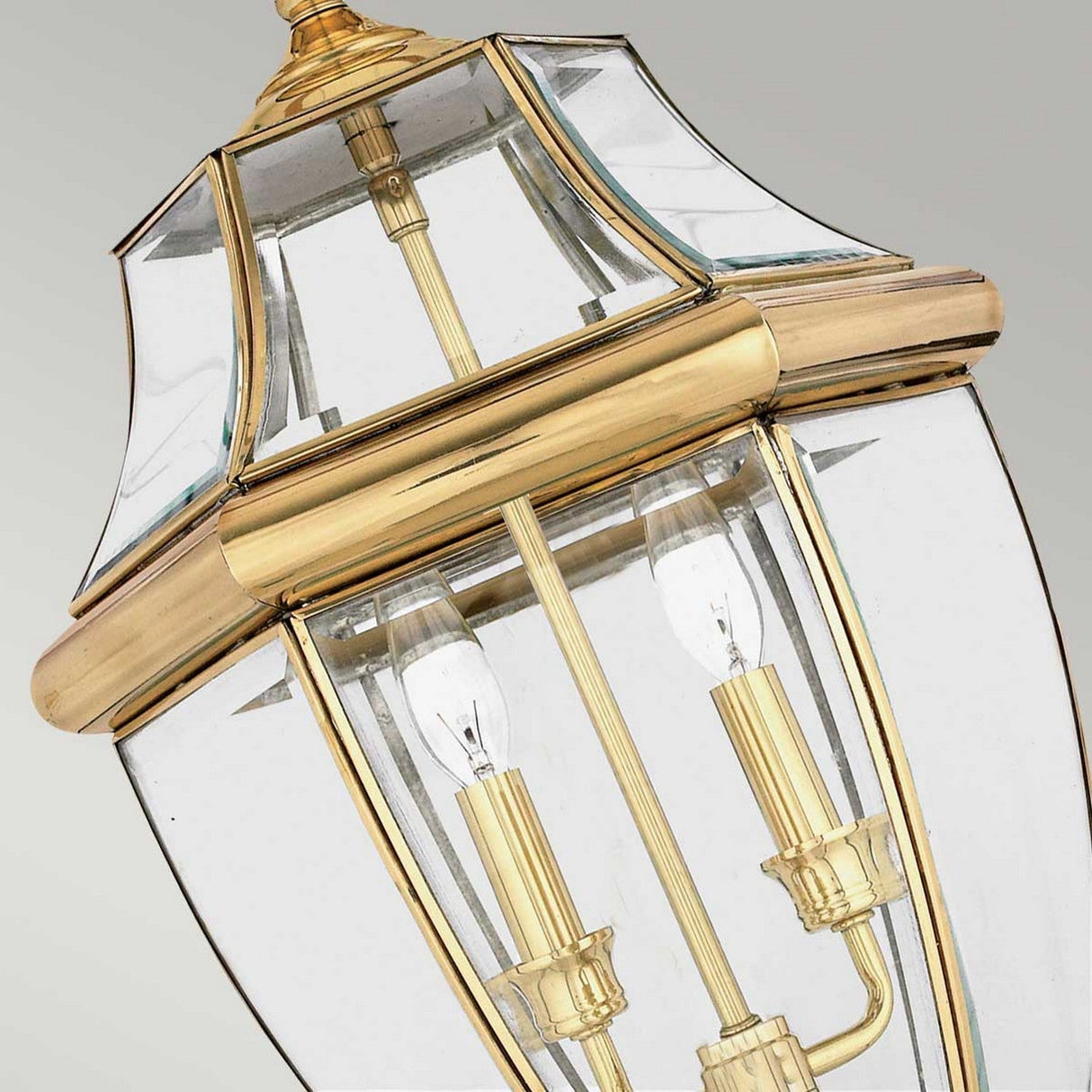 A close-up of the Newbury Outdoor 2 Light Large Chain Pendant reveals its elegant brass and glass design, featuring visible light bulbs. The pendant light showcases a lacquered polished brass finish and clear beveled glass panels, offering a sophisticated and timeless appearance.