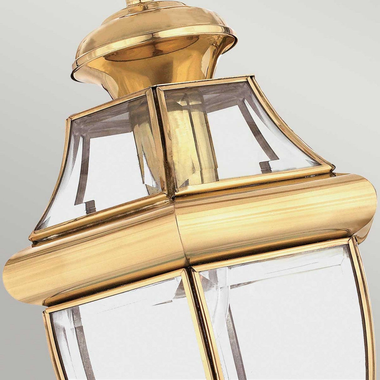 Close-up of the Newbury Outdoor 1 Light Medium Chain Pendant in lacquered polished brass, featuring elegant gold accents and clear beveled glass panels against a light gray background. This pendant showcases a classic design with clean lines and a decorative top.