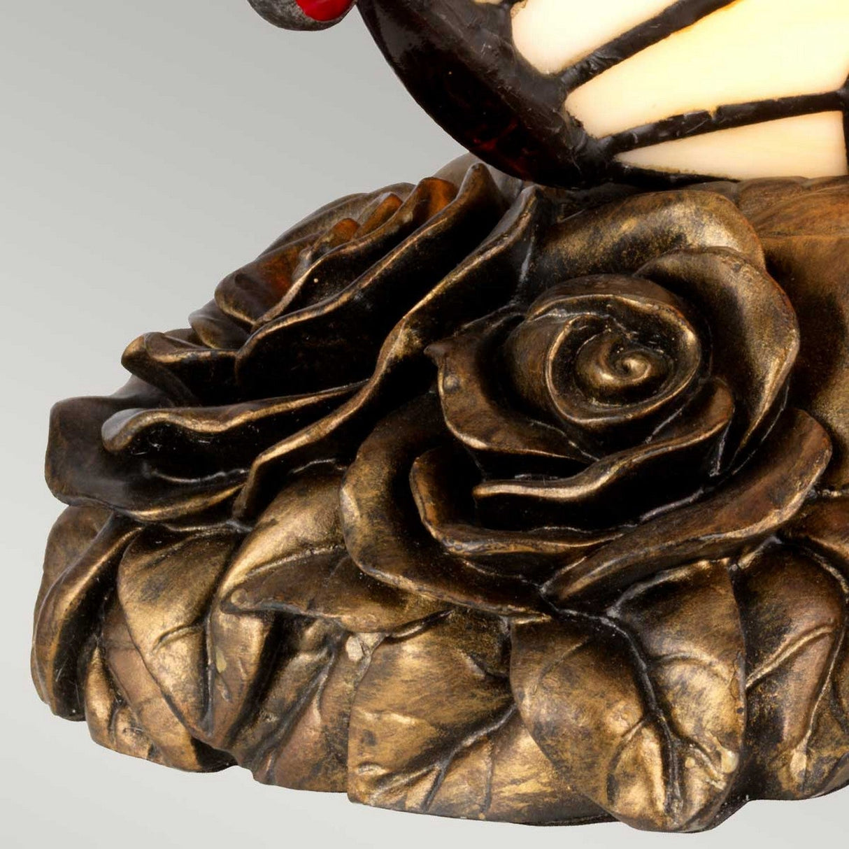 Close-up of the Tiffany Animal Lamps Orange Butterfly Lamp in architectural bronze, showcasing ornate design with detailed roses and leaves in relief. The craftsmanship emphasizes intricate textures and shading, echoing the artistry found in stained glass floral designs.